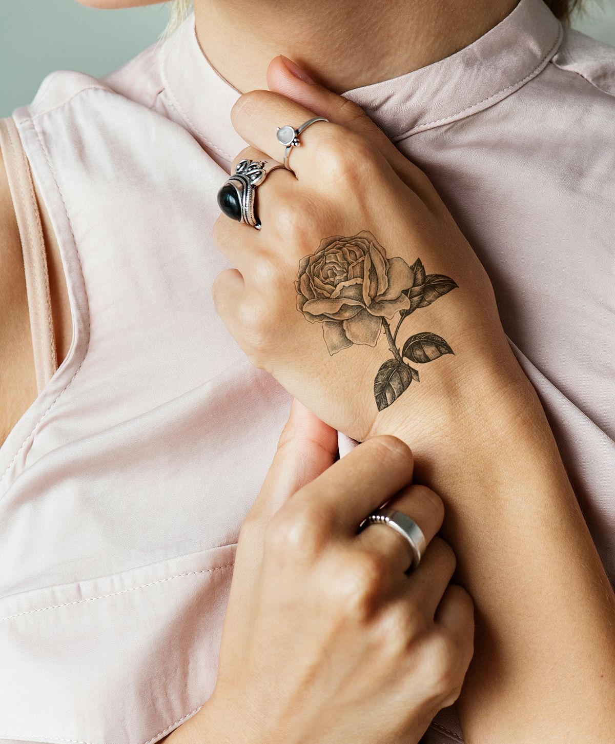 Hand with rose tattoo and silver rings.