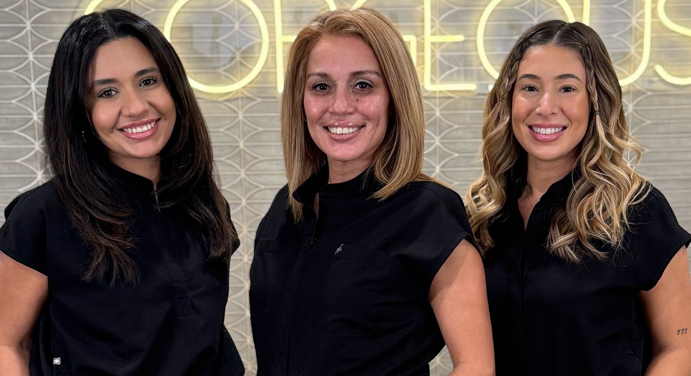 Three women smiling in black tops.