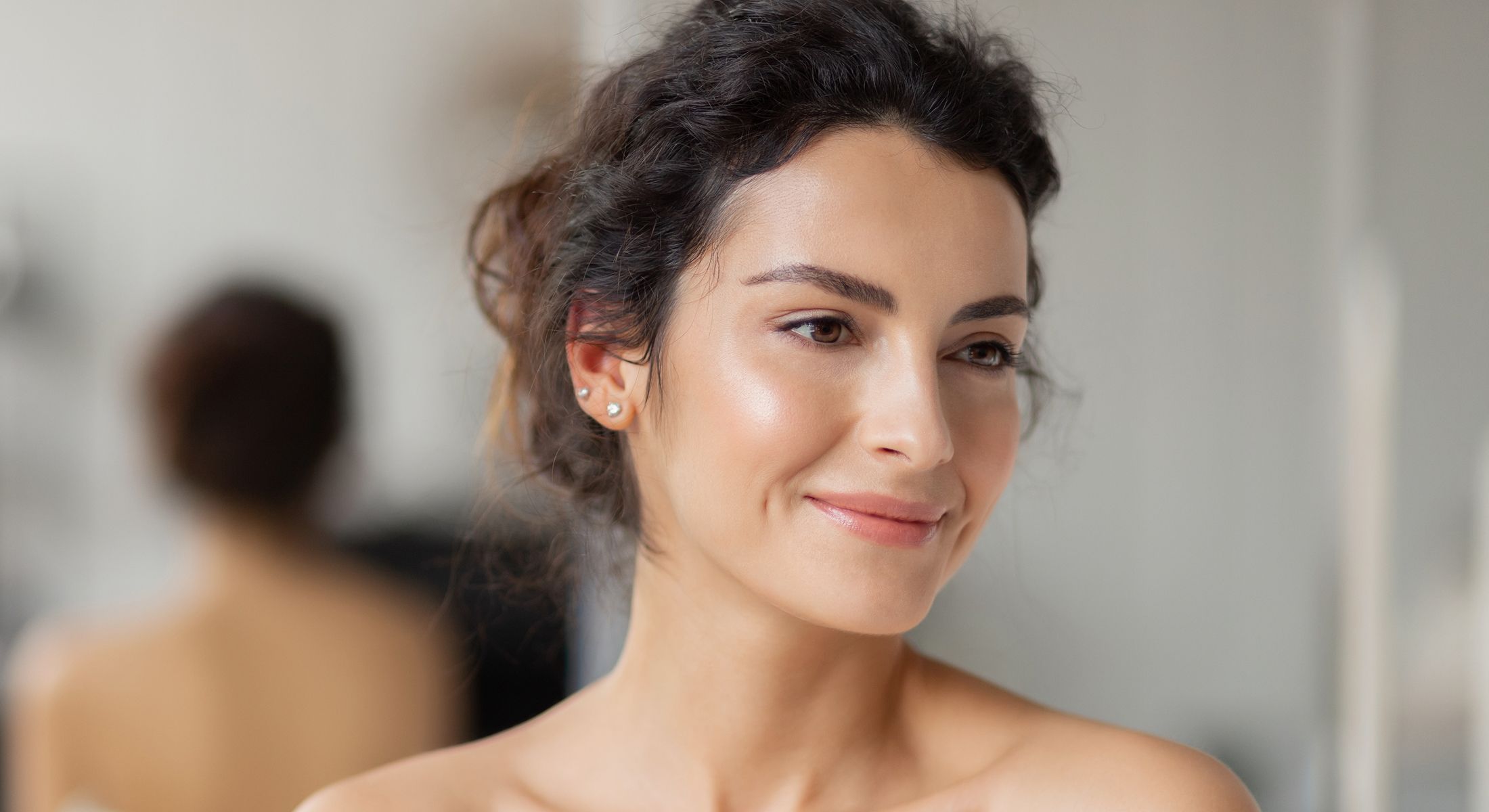 Woman applying skincare treatment, smiling in mirror.